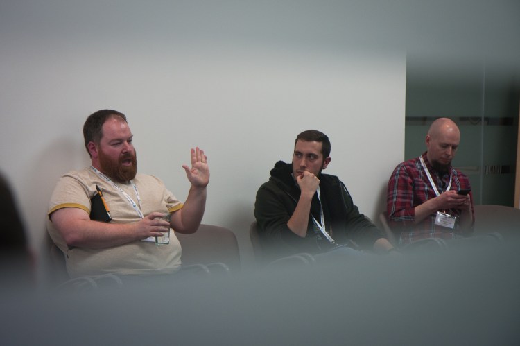 View through window at three people in a discussion, one has their hand up as they talk
