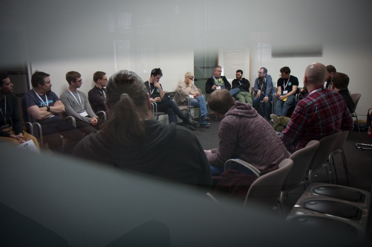 View through a window at a group of people sitting in a circle in a discussion